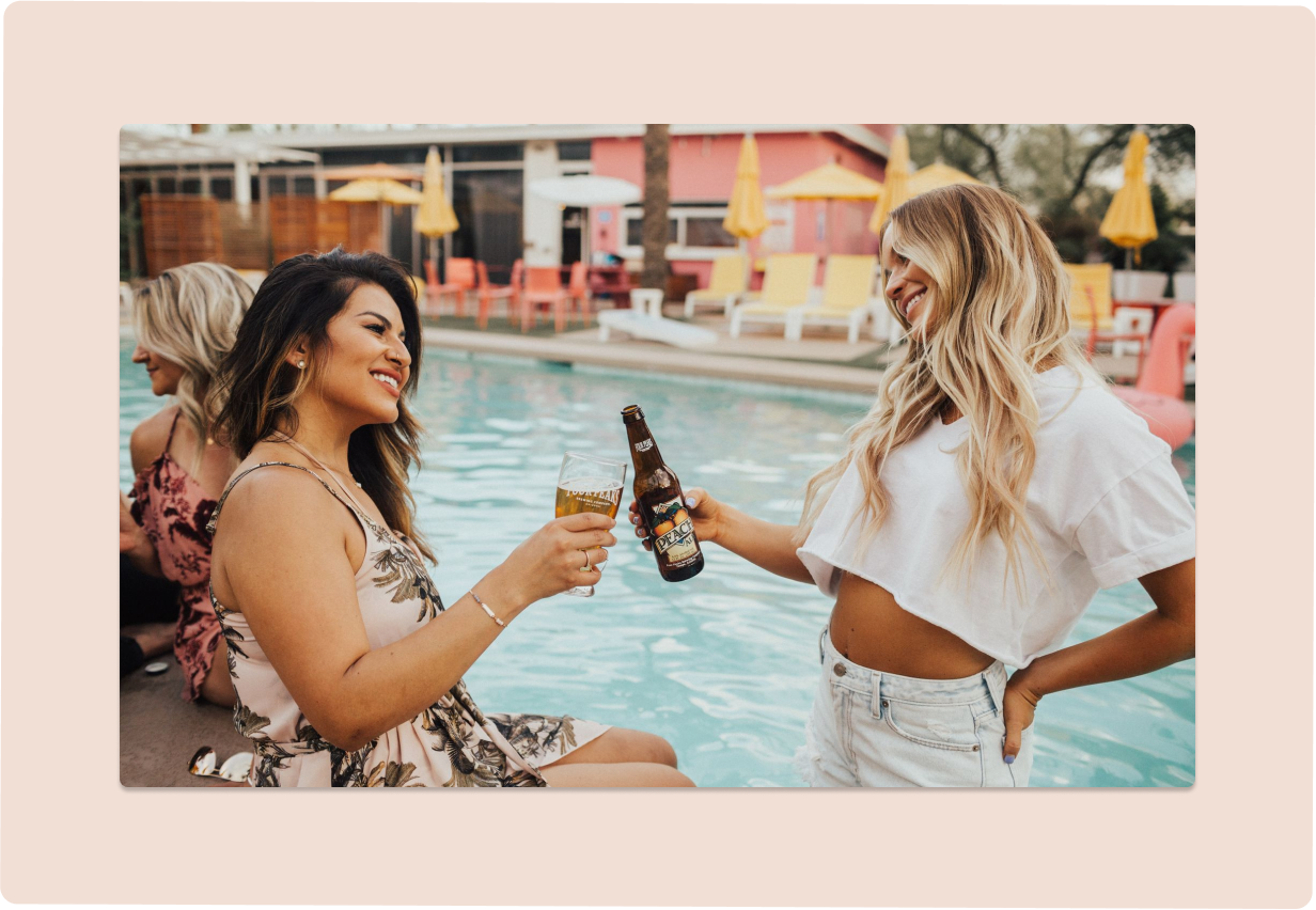 scene of two women drinking a beer by a pool