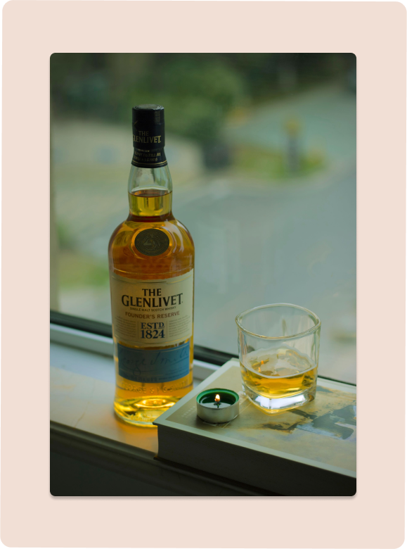 Whiskey, glass, and candle next to window