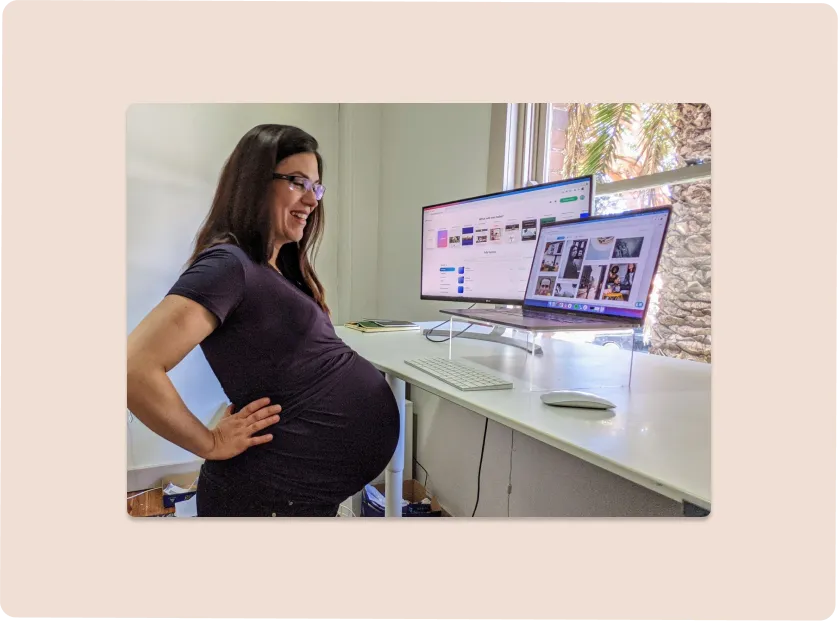 picture of a pregnant woman standing at her desk looking at computer screens