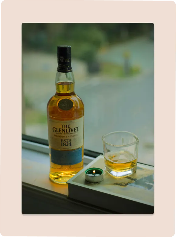 Whiskey, glass, and candle next to window